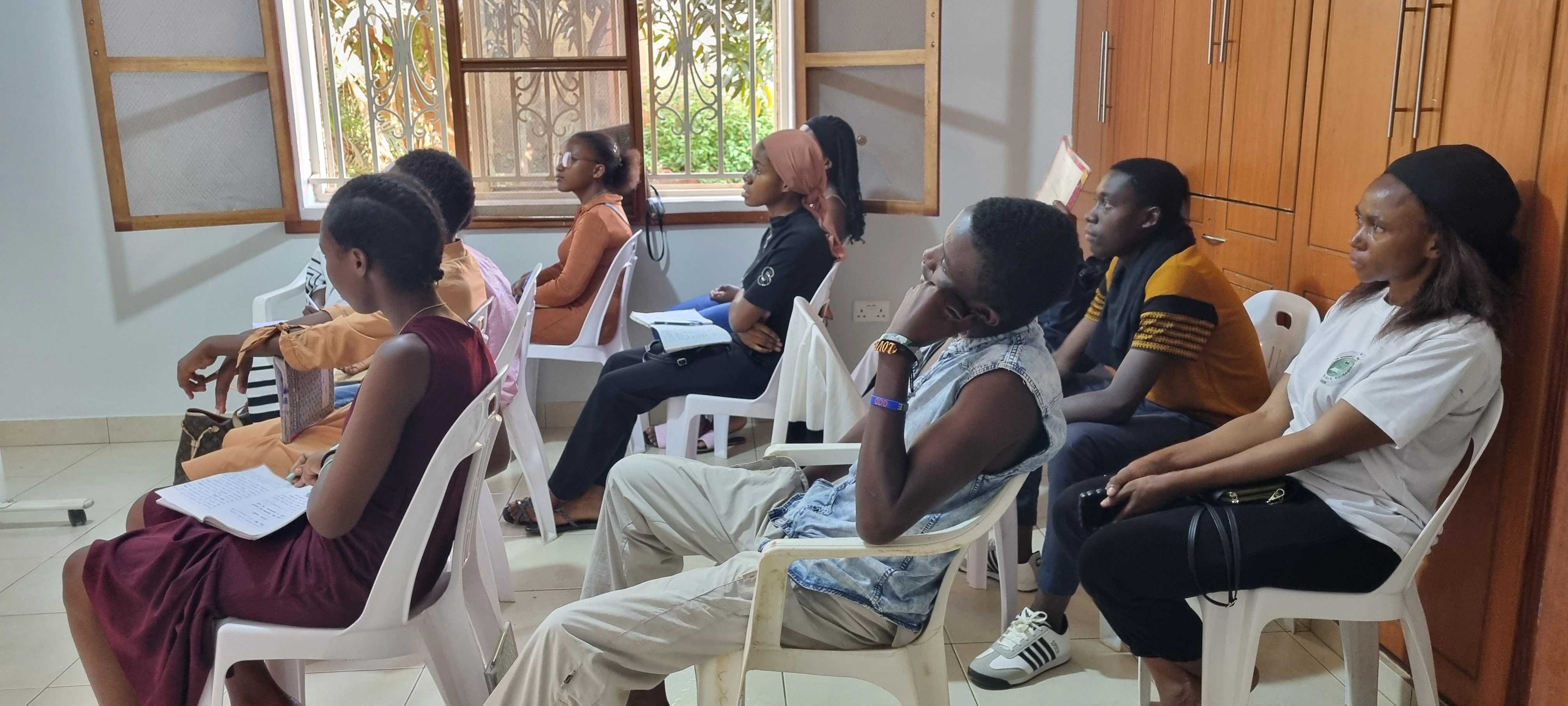 Young refugee learners listening closely during a YAREN English class, some holding notebooks