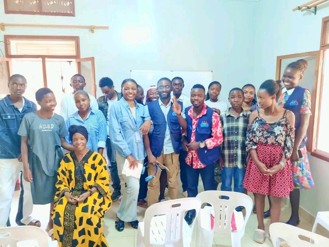 A smiling group of YAREN English learners and trainers in blue YAREN vests standing together in a classroom