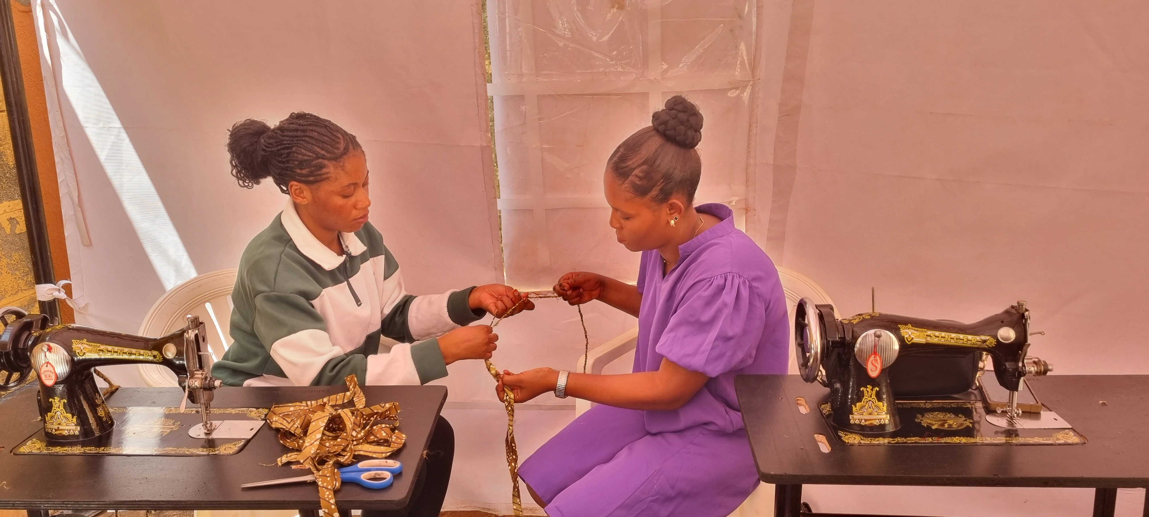 Two YAREN learners working together on a tailoring project between sewing machines